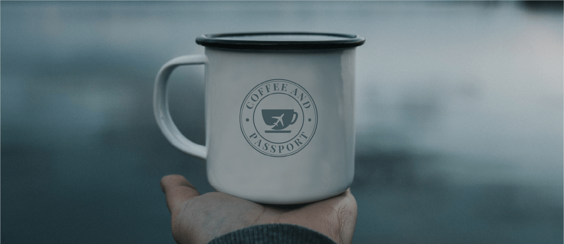 Brand Identity for Coffee and Passport on a mug, held in the palm of someone's hand on the shore of a lake.